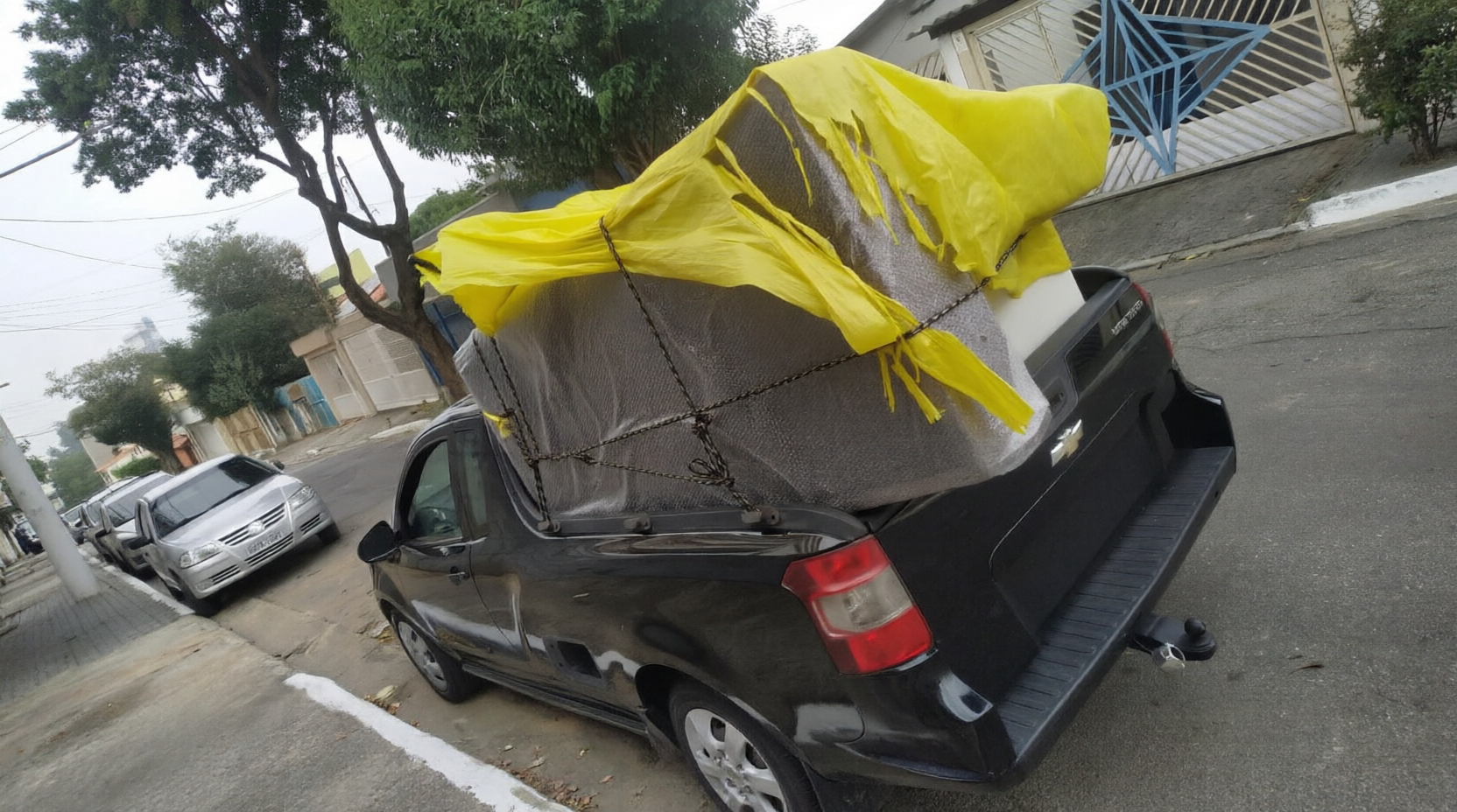 Colchão protegido com lona amarela e cordas de fixação na caminhonete